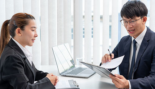 Conduct interviews - tycoonstory | tycoonstory media A business meeting where one person presents documents to another, illustrating a professional discussion during the hiring process, particularly when hiring your first employee.