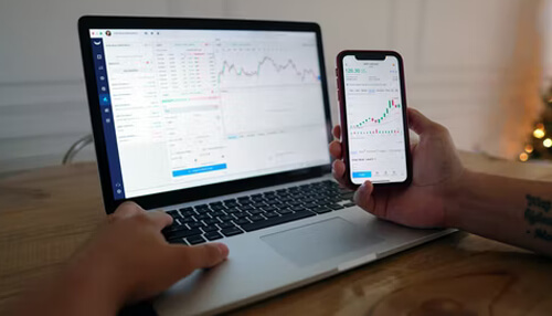Aggressive investors A person analyzing stock market charts on a laptop and smartphone, representing investing and tracking financial market performance.