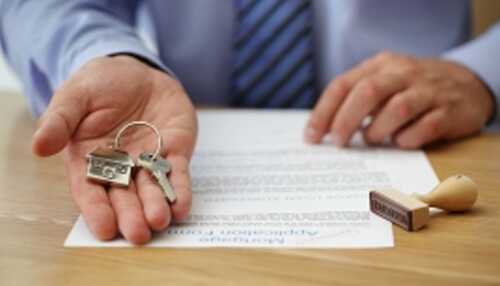 Digital lending retail lending Bank officer handing over house keys above a signed agreement, illustrating mortgage approval and retail lending services.