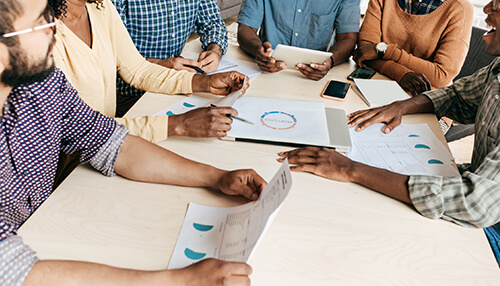 Group of professionals collaborating at a table, discussing data and charts during a marketing plan meeting Identify the market and competition for an outstanding marketing plan