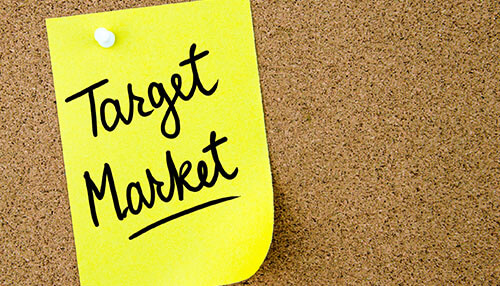 A yellow sticky note pinned to a corkboard with the text'Target Market' written on it Identify your target market to plan for your coaching business