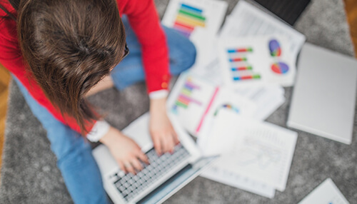 Improves workplace efficiency - tycoonstory | tycoonstory media Person operating laptop surrounded by scattered charts, with a being organized early to improve productivity and efficiency.