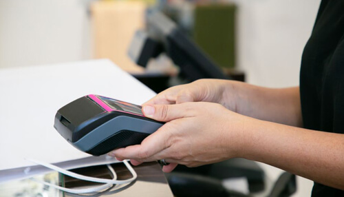 Payment processor when starting a business - tycoonstory | tycoonstory media A close-up of a hand holding a point-of-sale terminal, showing the use of a payment processor for processing card payments in a store.