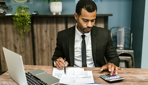 A businessman in a suit sitting at a desk, analyzing financial documents and using a calculator to manage his business accounts. Pricing calculation for your effective business proposal