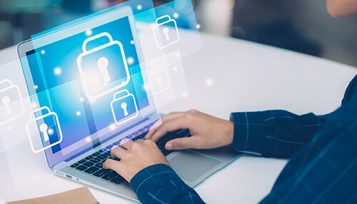 A person sitting with a laptop and typing is displayed with digital locks, which represent information security or data protection in cybersecurity.