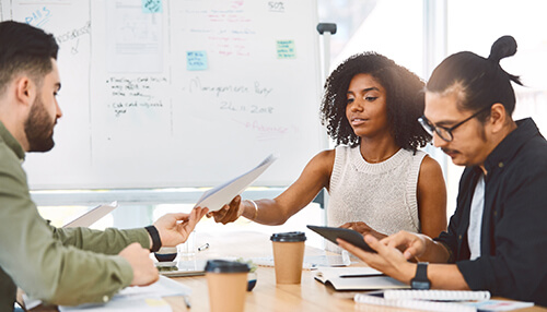 Track and evaluate marketing campaigns - tycoonstory | tycoonstory media Team collaborating in a meeting room, reviewing documents and digital reports related to web analytics on tablets and laptops