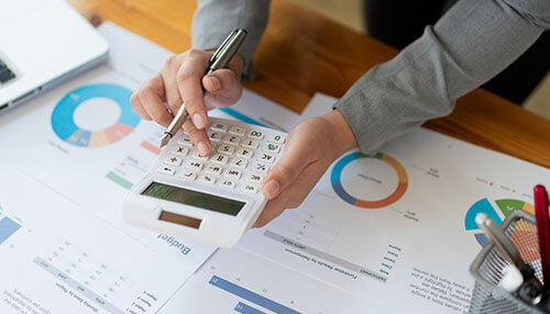 Average estimate Calculating customer lifetime value using a calculator while reviewing budget and sales charts on the table.