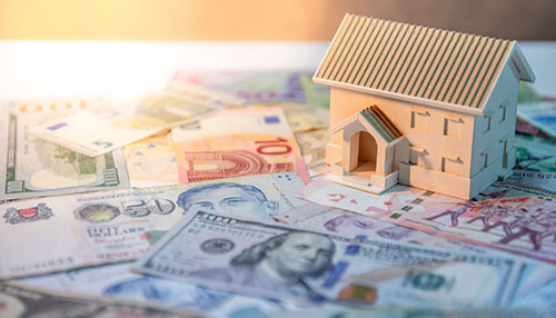 Dollars with real estate Model house placed on top of various international currencies, reflecting the financial success of real estate tycoons and investment opportunities.