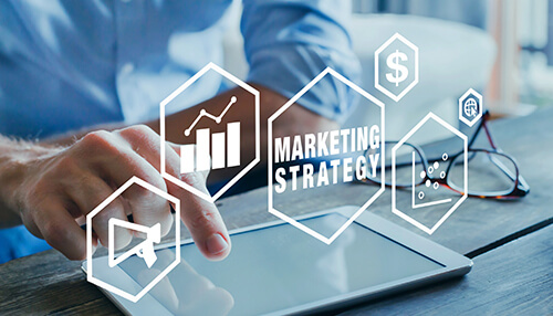 An economical marketing strategy Person using a tablet with digital icons representing promotional products marketing strategy, including graphs, dollar signs, megaphone, and analytics.