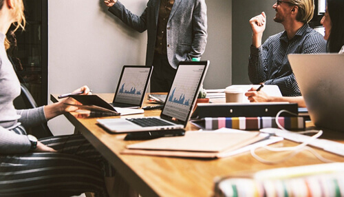 Be clear and concise when speaking Leader leading a meeting with a team, clearly explaining a concept while others listen attentively, under the topic'Be clear and concise when speaking.