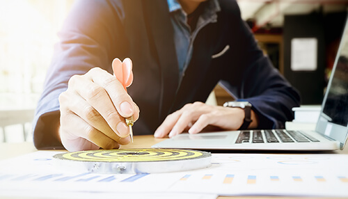 A business professional focuses intently on a target while using a laptop, illustrating the concept of goal setting and strategic planning for success. Choose the right business to maximize small business success
