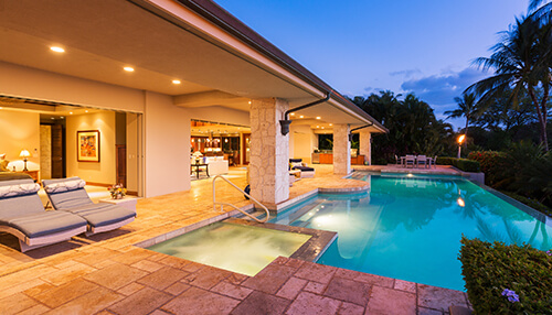 Consider the type of vacation rental - tycoonstory | tycoonstory media Luxurious poolside view of a modern vacation home with outdoor lounge chairs, pool, and tropical landscaping at sunset.