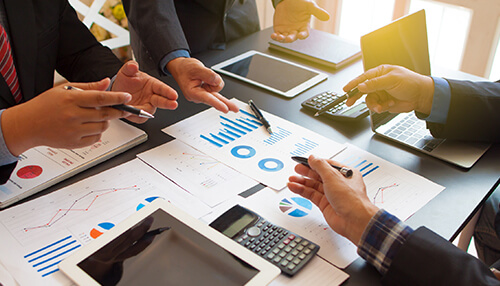 Decide on the investing strategy Business professionals analyzing charts and financial reports on a table with tablets and calculators, discussing strategies to build a strong investment portfolio.