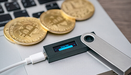 Different types of bitcoin digital wallets - tycoonstory | tycoonstory media A cold storage hardware wallet connected to a laptop alongside physical gold bitcoin coins, showcasing essential security tools for safely buying bitcoins.