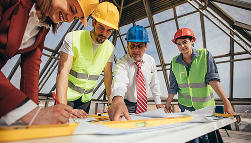Good communication is essential in every industry - tycoonstory | tycoonstory media Eam of engineers and workers reviewing building plans at a construction site, wearing safety helmets and vests, demonstrating safe construction practices.