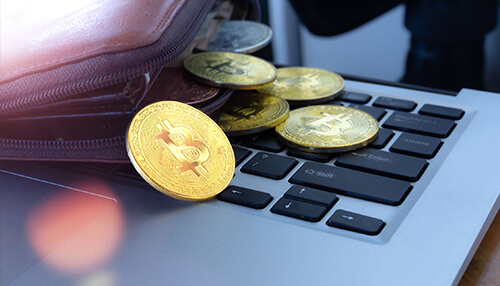 Overview of cryptographic wallets - tycoonstory | tycoonstory media Cryptocurrency coins, primarily bitcoin, spilling out of a wallet onto a laptop keyboard, symbolizing digital currency transactions.