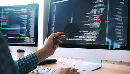 Phases of software development - tycoonstory | tycoonstory media A developer using a stylus to point at coding on a large screen, showcasing the software development process with multiple monitors displaying code.