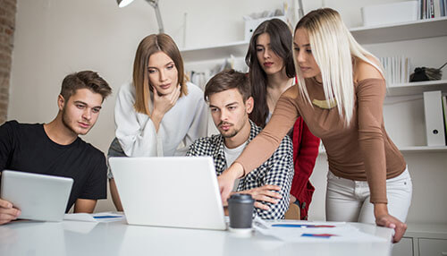 Group of employees collaborating on a project around a laptop, fostering teamwork and a positive work environment Promote communication and teamwork for a positive work environment