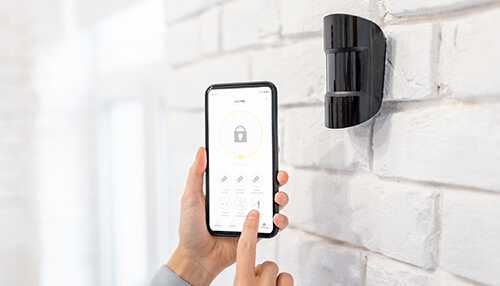 Set your business phone system home automation business User managing a wall-mounted security sensor using a smart app — home automation business security solutions.