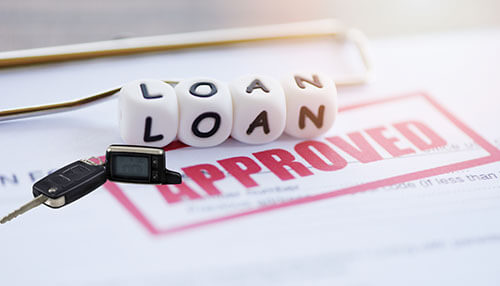 Value of a car as a collateral in loan approval - tycoonstory | tycoonstory media A hand moving a small red toy car across increasing stacks of coins next to a car key fob, symbolizing automotive financing and savings.