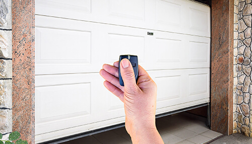 What to consider before installing a garage door - tycoonstory | tycoonstory media Hand using a remote control to operate an automatic garage door at home for easy and secure access.