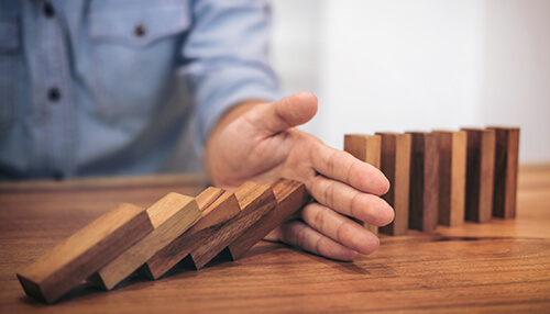 Your levels of risk - tycoonstory | tycoonstory media Liability insurance risk management concept showing hand stopping falling wooden blocks to prevent financial loss.