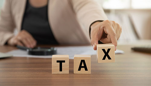 Tax implications A person arranging wooden blocks spelling “tax” on a desk, symbolizing financial planning and tax implications related to retirement accounts during divorce.