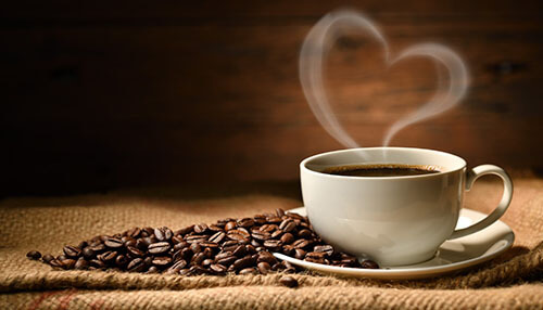 Coffee mugs Warm café setting with a steaming cup of coffee on a rustic table, surrounded by roasted coffee beans and heart-shaped steam.