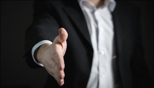 Be creative and open-minded - tycoonstory | tycoonstory media A close-up of a business professional extending a handshake, symbolizing a strong display of business acumen in establishing trust and collaboration.