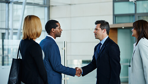 Build a relationship Two business professionals shaking hands while two others observe in a modern office environment.