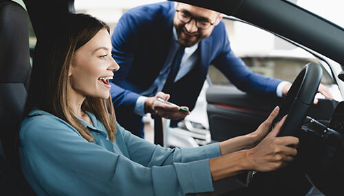 Private sellers Happy woman test driving a car with a salesman, demonstrating the joy of buying a used car.