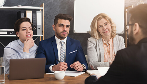 Conduct interviews A team of professionals sitting around a table, conducting an interview, reflecting a structured process in a robust recruitment policy.