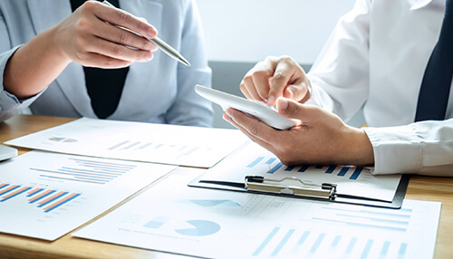 Determine the success of your brand in your business markets Two professionals discussing market research findings, using tablets and papers with bar graphs and pie charts to analyze key insights.