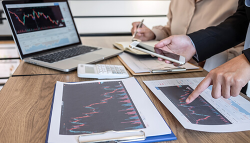 Morningstar - tycoonstory | tycoonstory media Professionals at a desk with a laptop discussing motley fool vs. Morningstar strategies while analyzing stock charts.