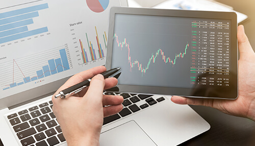 Motley fool - tycoonstory | tycoonstory media Close-up of hands analyzing financial charts on a tablet and laptop, with graphs and stock data on the screens.