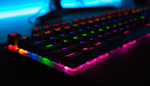 Playing online games Close-up of a colorful rgb mechanical keyboard glowing in the dark, symbolizing hobbies like gaming and how they can help develop entrepreneurial skills.