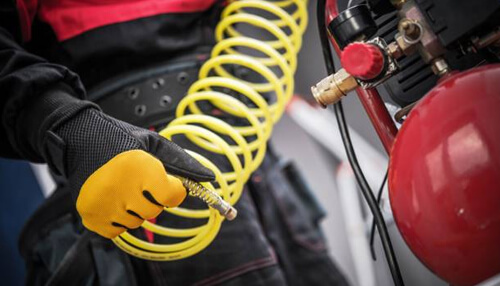Regularly clean the air compressor Worker holding a yellow air hose connected to a red air compressor, preparing for industrial use.