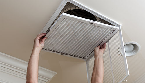 Air filter installation mistakes Person installing a clean air filter into a ceiling return vent as part of home hvac maintenance.
