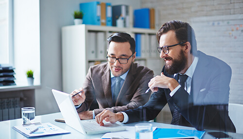 Benefits of blockchain consulting Two business professionals discussing data on a laptop during a blockchain consulting session in an office setting