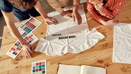 Custom stickers Designers brainstorming over a t-shirt layout and color palettes, illustrating the creation of custom stickers for branding and promotional purposes.