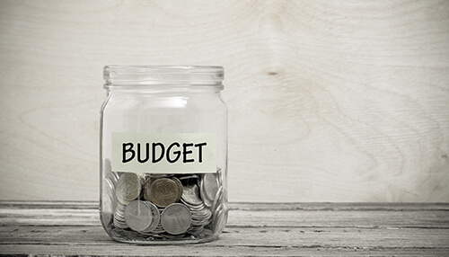 Consider your budget Glass jar labeled budget filled with coins on a wooden table