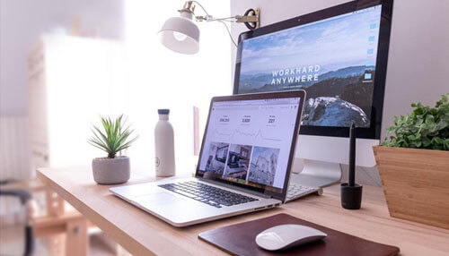 Create and optimize an unmatched website Minimalist workspace featuring a laptop, desktop monitor with a motivational'Work Hard Anywhere' background, plants, and a mouse, symbolizing productivity and remote work.