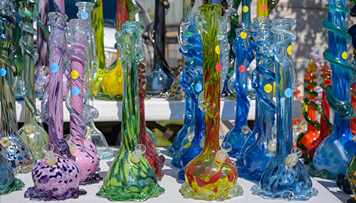 How long does glow in the dark last - tycoonstory | tycoonstory media A colorful assortment of intricate glow in the dark glass bongs sits on the table under sunlight, showing several shapes and patterns.