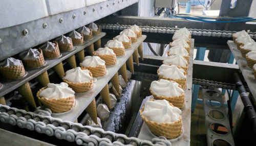 Food manufacturing business ideas Ice cream cones being filled and processed on a production line, demonstrating food manufacturing business ideas in the dessert sector.