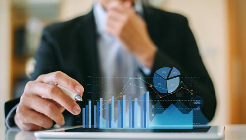 Look at market opportunities Laptop screen displaying code editor with programming language syntax. A stack of books is visible next to the laptop against a sun-dappled wall, representing the technical aspect of working in a business in development or tech.