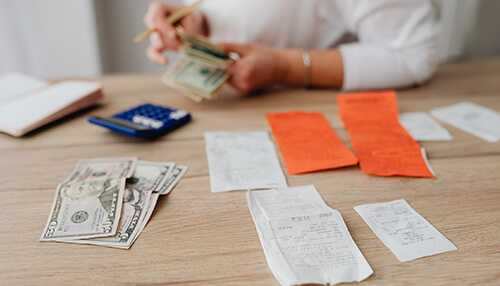 Pay all bills in writing Person counting cash and reviewing receipts at a desk with a calculator, illustrating financial management and bookkeeping.