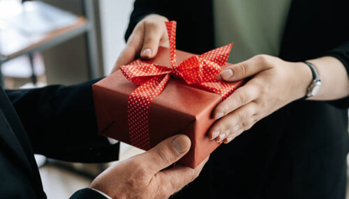 Quality A businessperson handing over a carefully wrapped gift with a red ribbon, symbolizing the exchange of thoughtful gifts for business to foster goodwill