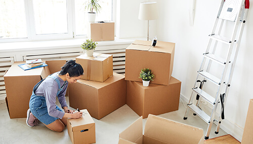 Take a good look at relocation benefits Woman labeling moving boxes at home, organizing her life during a career shift.
