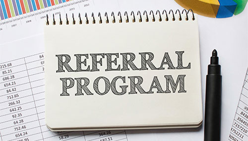 Create a referral program Notebook labeled “referral program” placed on business reports and charts, symbolizing how a team collaborates to build referral strategies and drive growth.