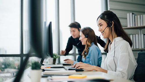 Agent assistance tools - tycoonstory | tycoonstory media Customer support agents, wearing headsets, in a contact center using agent assistance tools with a supervisor in the background.